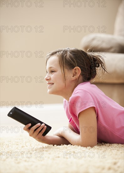 Girl (10-11) lying on floor holding remote control. Photo : Mike Kemp
