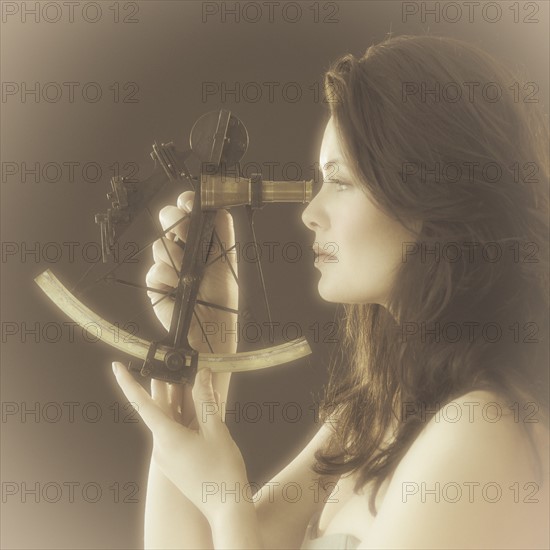 Woman looking through antique sextant, world map in background.