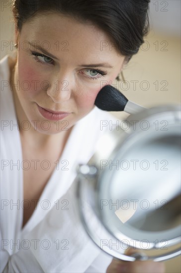 Woman applying blush on cheekbones.