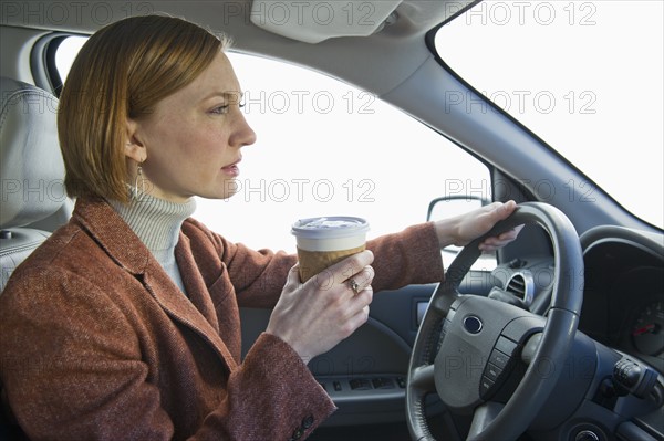 Woman driving car and drinking coffee.