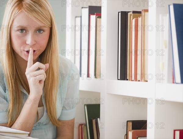 Female student in library holding finger on lips. Photo: Jamie Grill Photography