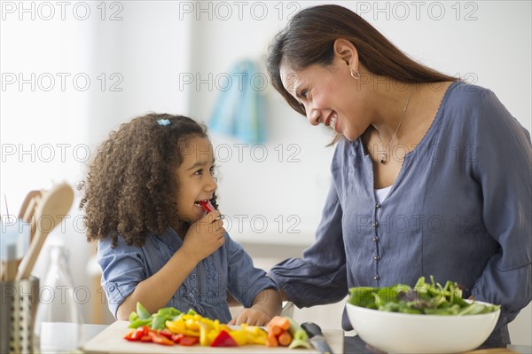 Mother with daughter (6-7) preparing food in kitchen.
