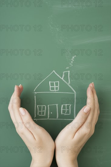 Woman holding hands around house drawn on blackboard.