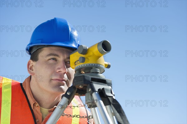Construction worker in hard hat using theodolite.