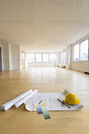 Blueprint, color swatch and hardhat on floor in empty room.