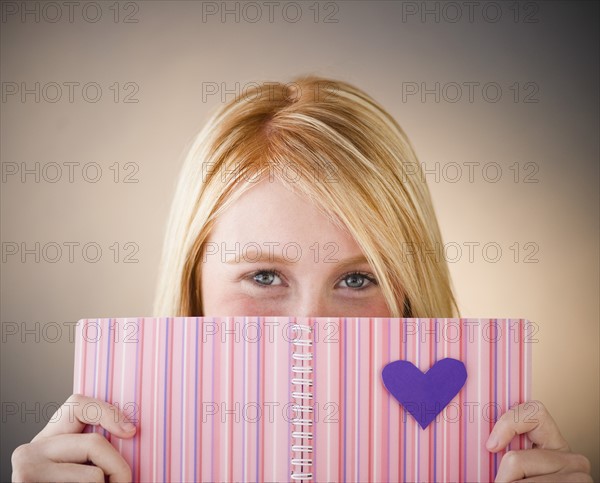 Young woman hiding behind diary. Photo : Jamie Grill Photography