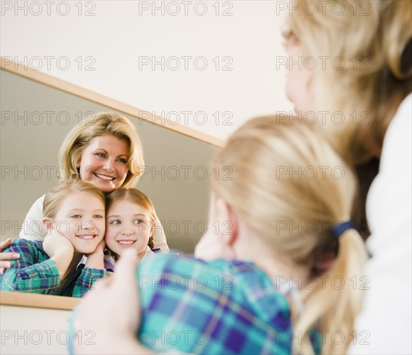 Mother and daughters (8-11) looking into mirror. Photo : Jamie Grill Photography