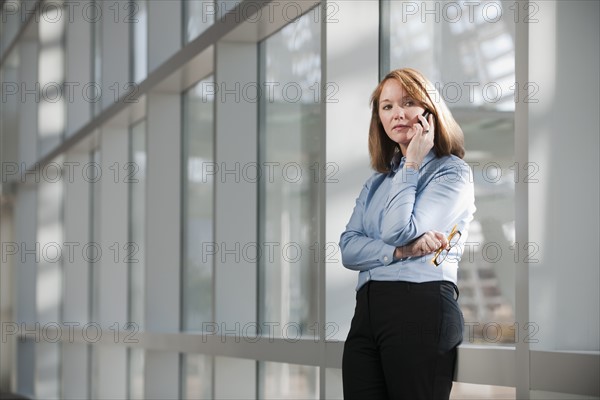 Businesswoman talking on phone in corridor. Photo : Mark Edward Atkinson