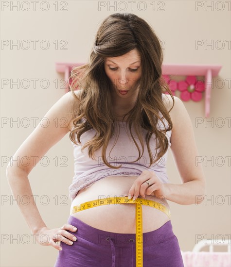 Young pregnant woman measuring belly. Photo : Mike Kemp