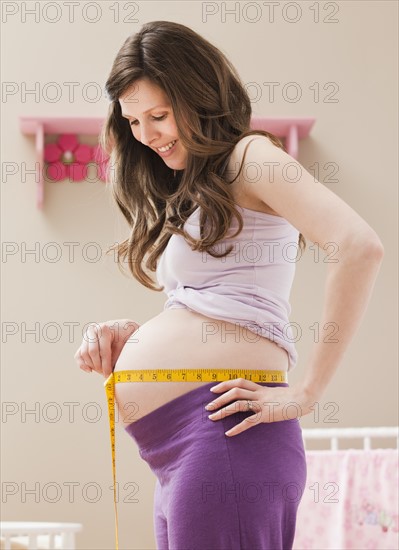 Young pregnant woman measuring belly. Photo : Mike Kemp