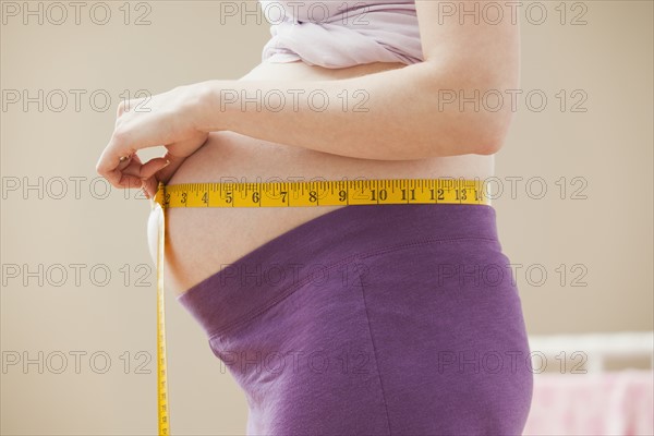 Young pregnant woman measuring belly. Photo : Mike Kemp