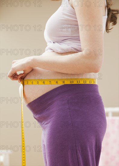 Young pregnant woman measuring belly. Photo : Mike Kemp