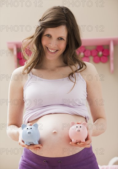 Young pregnant woman holding blue and pink piggybanks. Photo : Mike Kemp