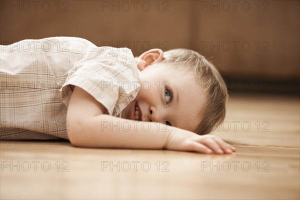 Portrait of smiling boy (2-3) lying on floor. Photo : Mike Kemp