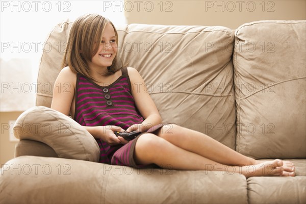 Girl (10-11) sitting on sofa, watching TV. Photo : Mike Kemp