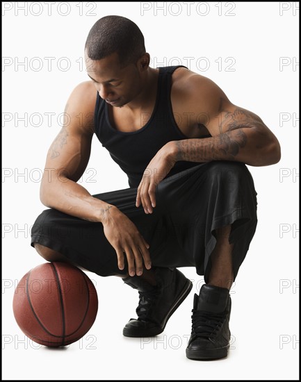 Studio shot of man with basketball crouching. Photo : Mike Kemp