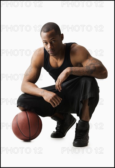 Studio shot of man with basketball crouching. Photo : Mike Kemp