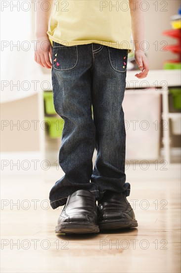 Girl (2-3) standing in dad's shoes, low section. Photo : Mike Kemp