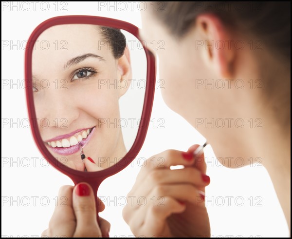 Studio portrait of young woman applying lipstick in mirror. Photo: Mike Kemp