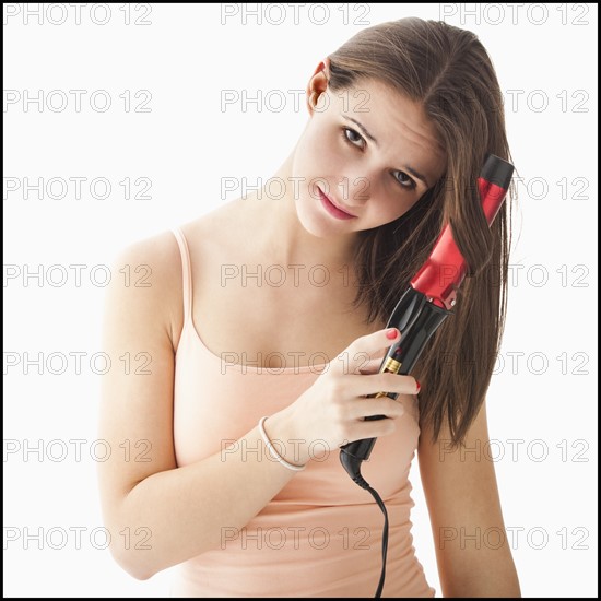 Studio portrait of young woman curling hair. Photo : Mike Kemp