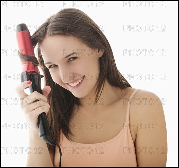 Studio portrait of young woman curling hair. Photo : Mike Kemp