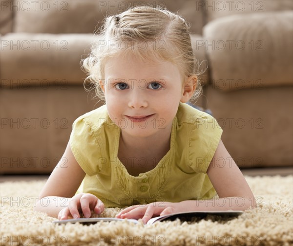 Portrait of smiling girl (2-3) lying on rug with book. Photo : Mike Kemp