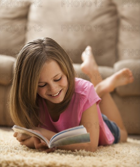 Girl (10-11) lying on rug, reading book. Photo: Mike Kemp