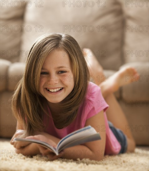 Portrait of girl (10-11) lying on rug with book. Photo: Mike Kemp