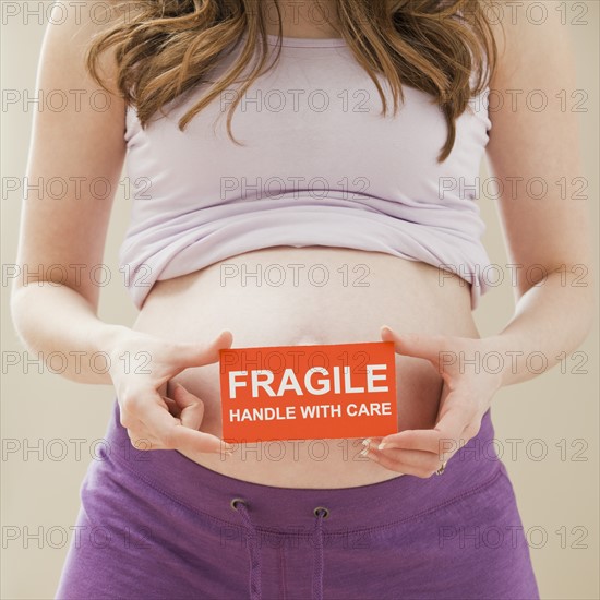 Young pregnant woman holding fragile sign. Photo : Mike Kemp