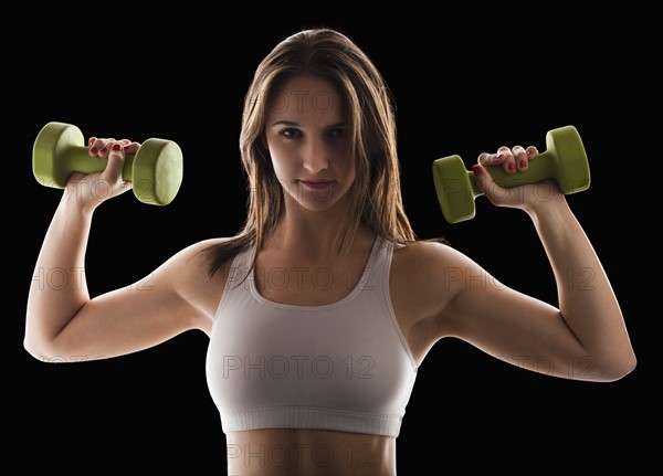 Studio portrait of young woman using hand weights. Photo : Mike Kemp