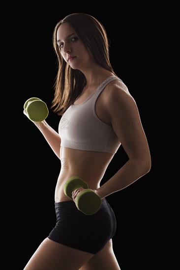 Studio portrait of young woman using hand weights. Photo: Mike Kemp