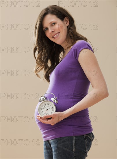 Young pregnant woman holding alarm clock next to belly. Photo: Mike Kemp