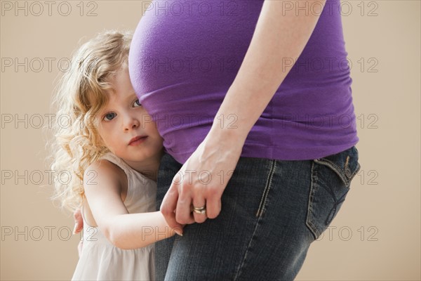 Girl (2-3) peeking form behind pregnant mother's belly. Photo : Mike Kemp