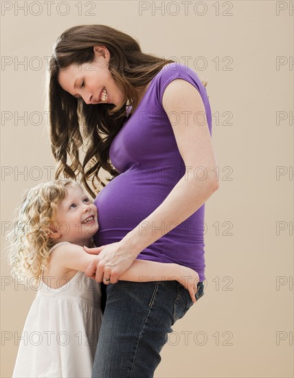 Portrait of girl (2-3) and pregnant mother embracing. Photo: Mike Kemp