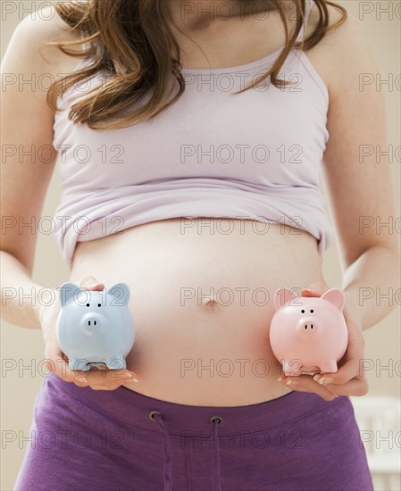 Young pregnant woman holding blue and pink piggybanks. Photo : Mike Kemp