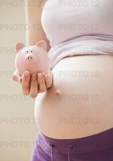 Young pregnant woman holding pink piggybank. Photo : Mike Kemp