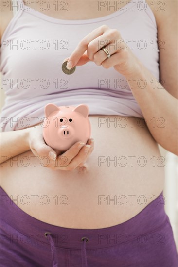Young pregnant woman putting coin into pink piggybank. Photo: Mike Kemp