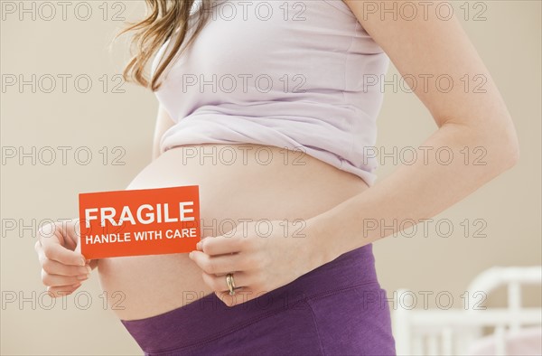 Young pregnant woman holding fragile sign. Photo : Mike Kemp