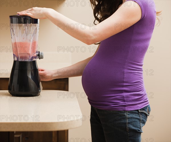 Young pregnant woman using juice extractor. Photo: Mike Kemp