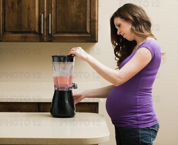 Young pregnant woman using juice extractor. Photo : Mike Kemp