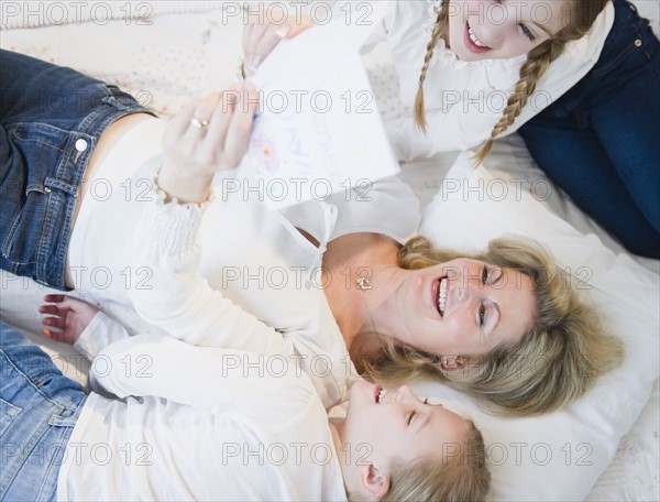 Mother and daughters (8-11) reading letter on bed. Photo: Jamie Grill Photography