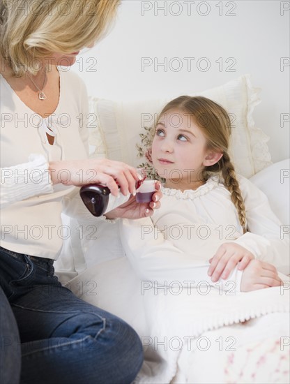 Mother giving medication to daughter (10-11) in bed. Photo: Jamie Grill Photography