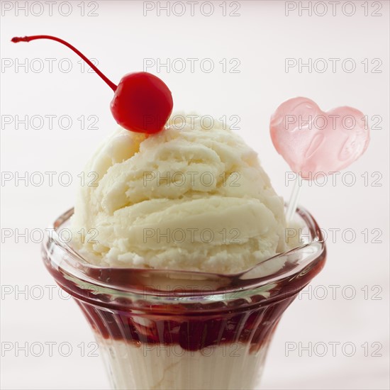 Close up of ice cream dessert with cherry on top and heart shaped decoration.