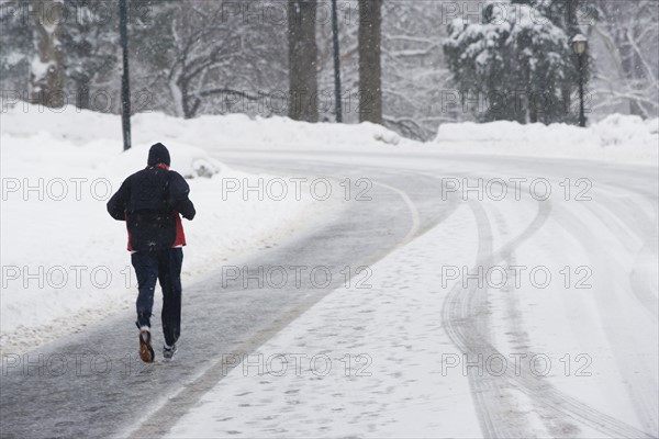 USA, New York City, man jogging up snowy road. Photo: fotog