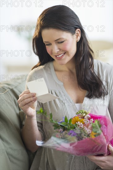 Young woman holding bouquet and reading greeting card.