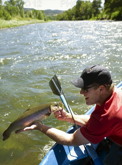 USA, Colorado, Man sitting in fishing boat, holding large trout. Photo : John Kelly