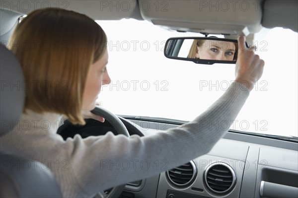 Woman driving car and adjusting mirror.