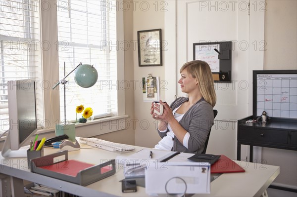 Woman sitting in office room, holding cup of tea. Photo : DreamPictures