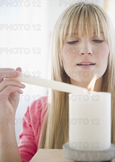 Young woman igniting candle. Photo : Jamie Grill Photography