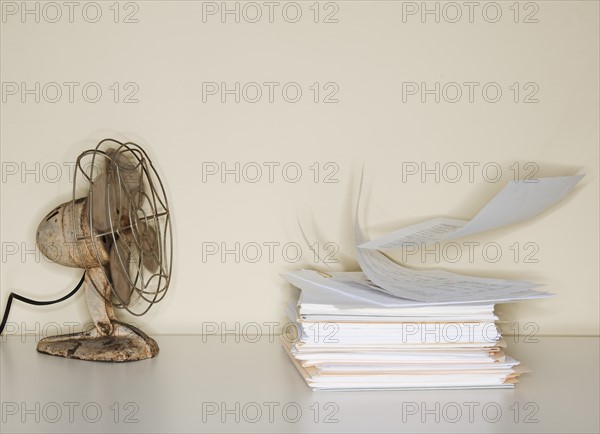 Electric fan blowing on heap of papers.
